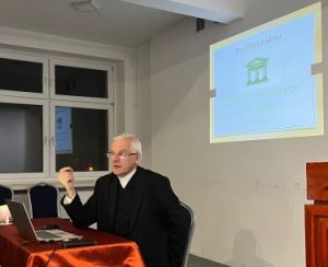 ks. prof. UAM dr hab. Maciej Olczyk siedząc przy stole przemawia do słuchaczy