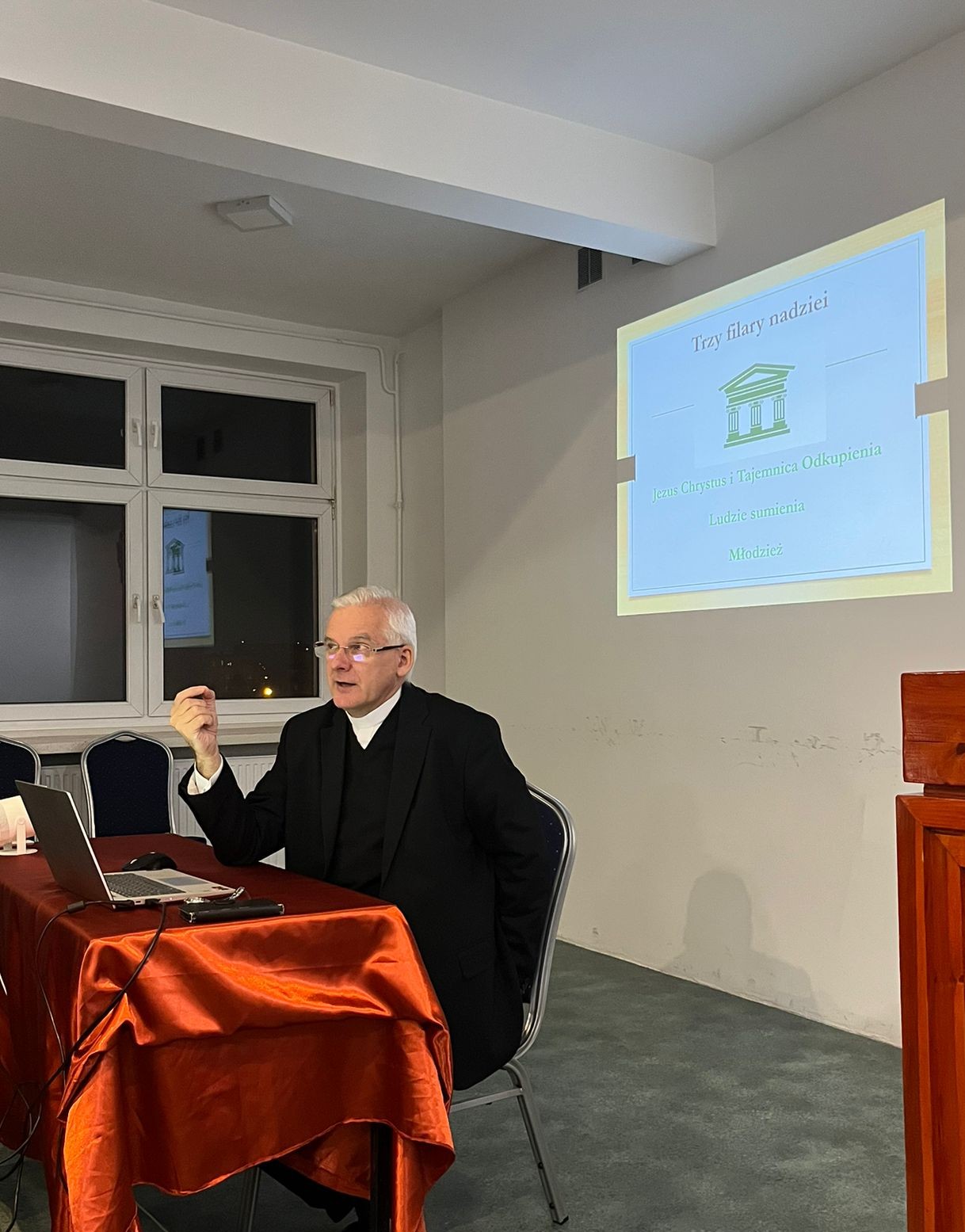 ks. prof. UAM dr hab. Maciej Olczyk siedząc przy stole przemawia do słuchaczy